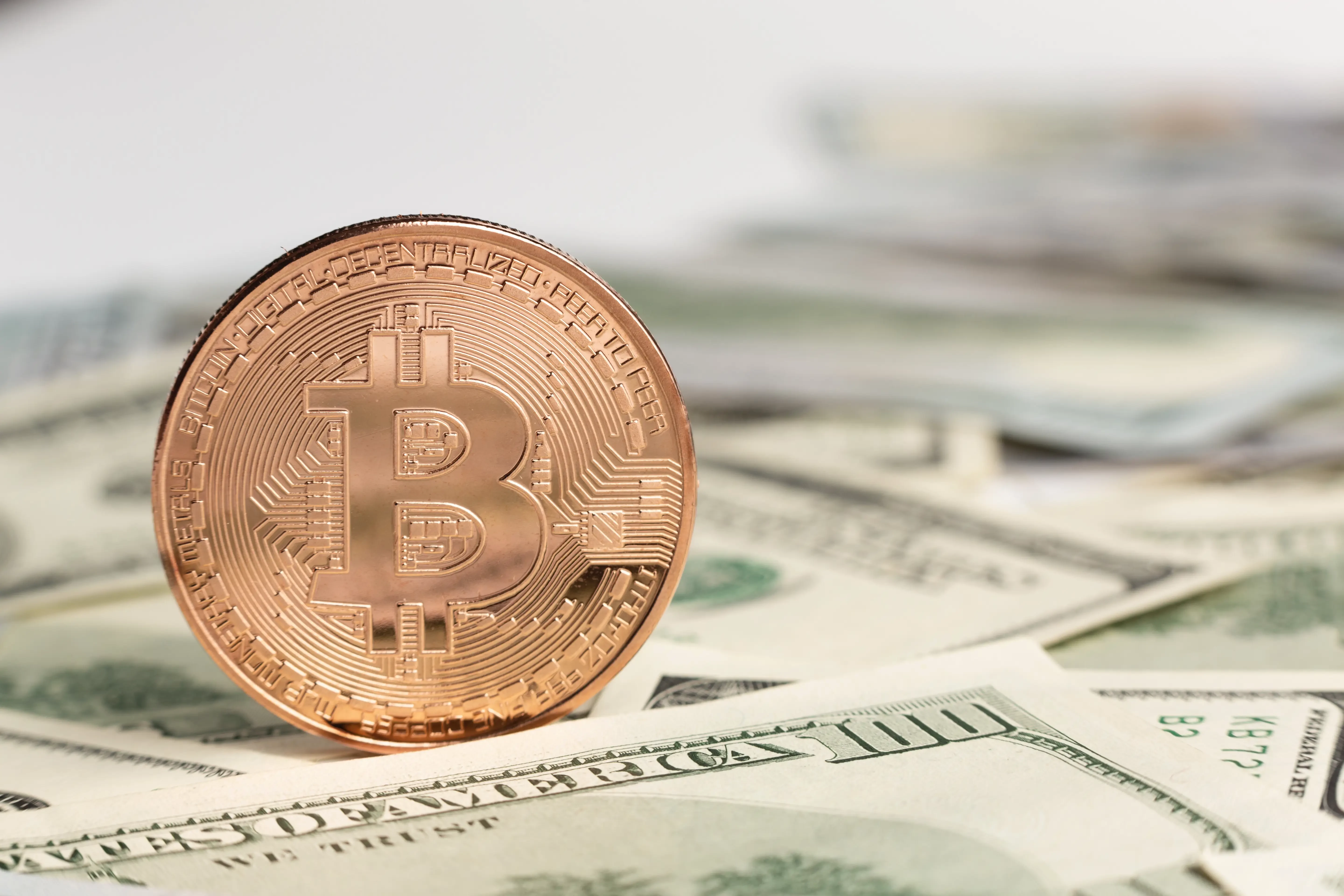 Fotografia de uma bitcoin em cima de vários dólares